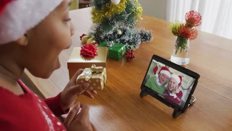 Mujer-Afroamericana-Con-Sombrero-De-Santa-Usando-Tableta-Para-Videollamada-Navideña-Con-Pareja-En-Pantalla