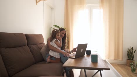 smiling mother and daughter using netbook on sofa at home