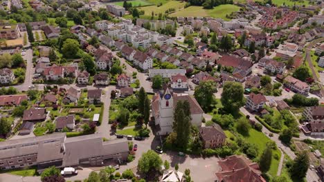 Historic church tower in Hinwil a swiss town in summer. Aerial top down orbit shot. Red roofs of houses and luxury apartment Blocks in Switzerland. Green grass and trees.