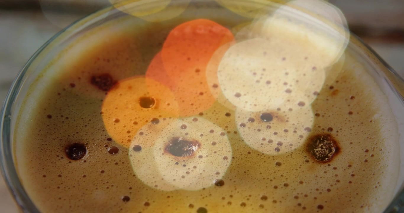 Tazza di caffè che mostra un bokeh caldo e sfocato che si sposta da sinistra, rivelando la crema e suggerendo un movimento delicato.