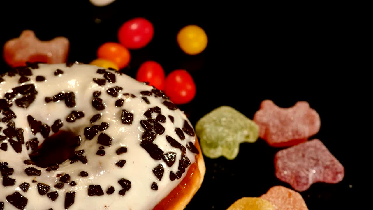 rosquilla blanca con chocolate, glaseado o salpicaduras, dulces de caramelo a rayas, dragee de colores con pasas o cacahuetes en el interior sobre un fondo negro