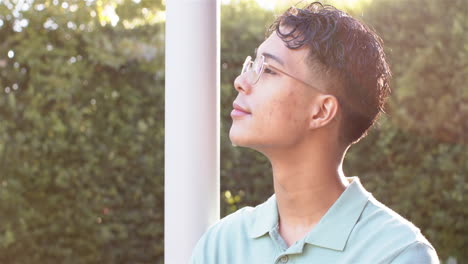 man with glasses standing outdoors, looking up and enjoying sunlight
