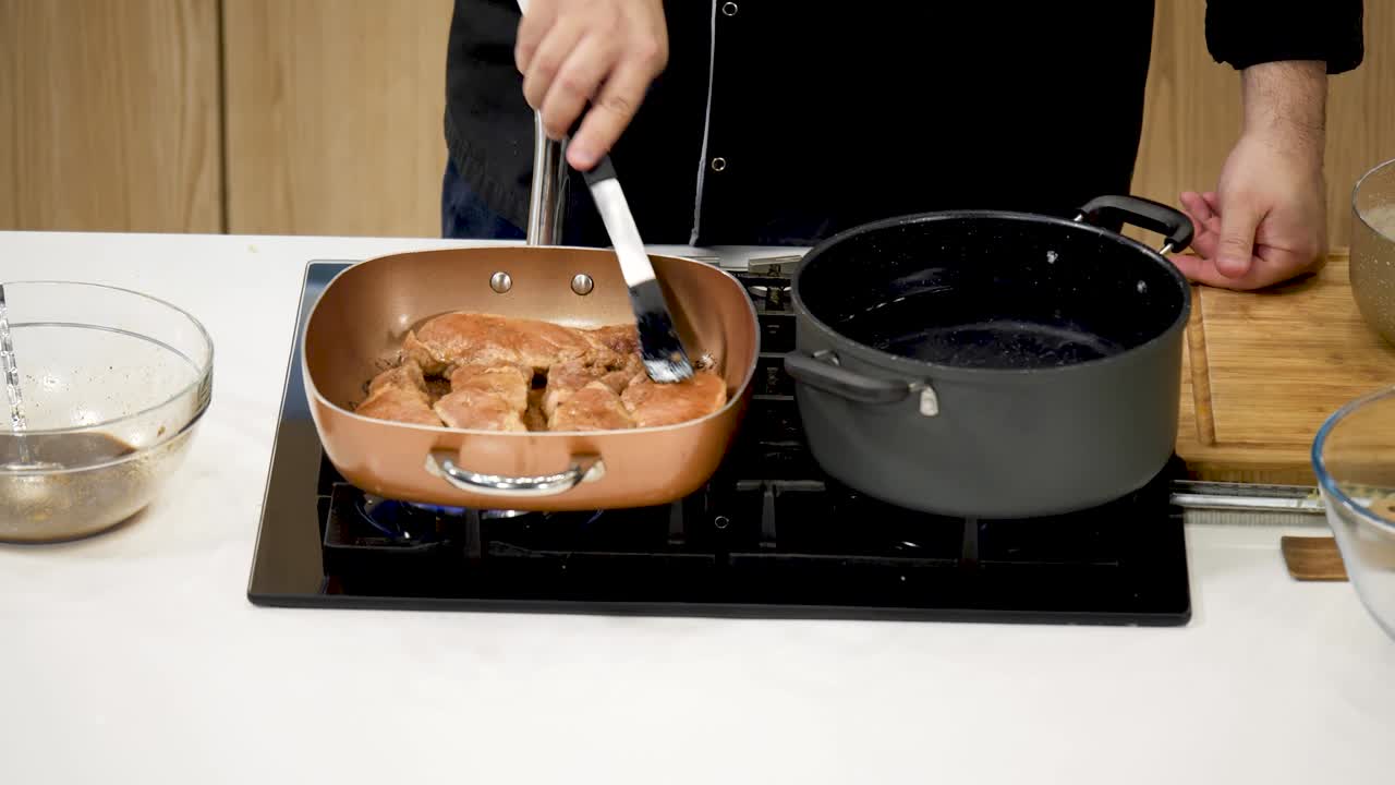 Chef in black uniform fries pork steaks in a frying pan, close-up. The man fries the meat on both sides until golden brown. The process of creating a dish in a restaurant kitchen