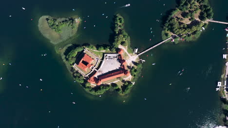 aerial: very high altitude top view of trakai island castle with boats sailing around it and visible isolated islands with growing trees