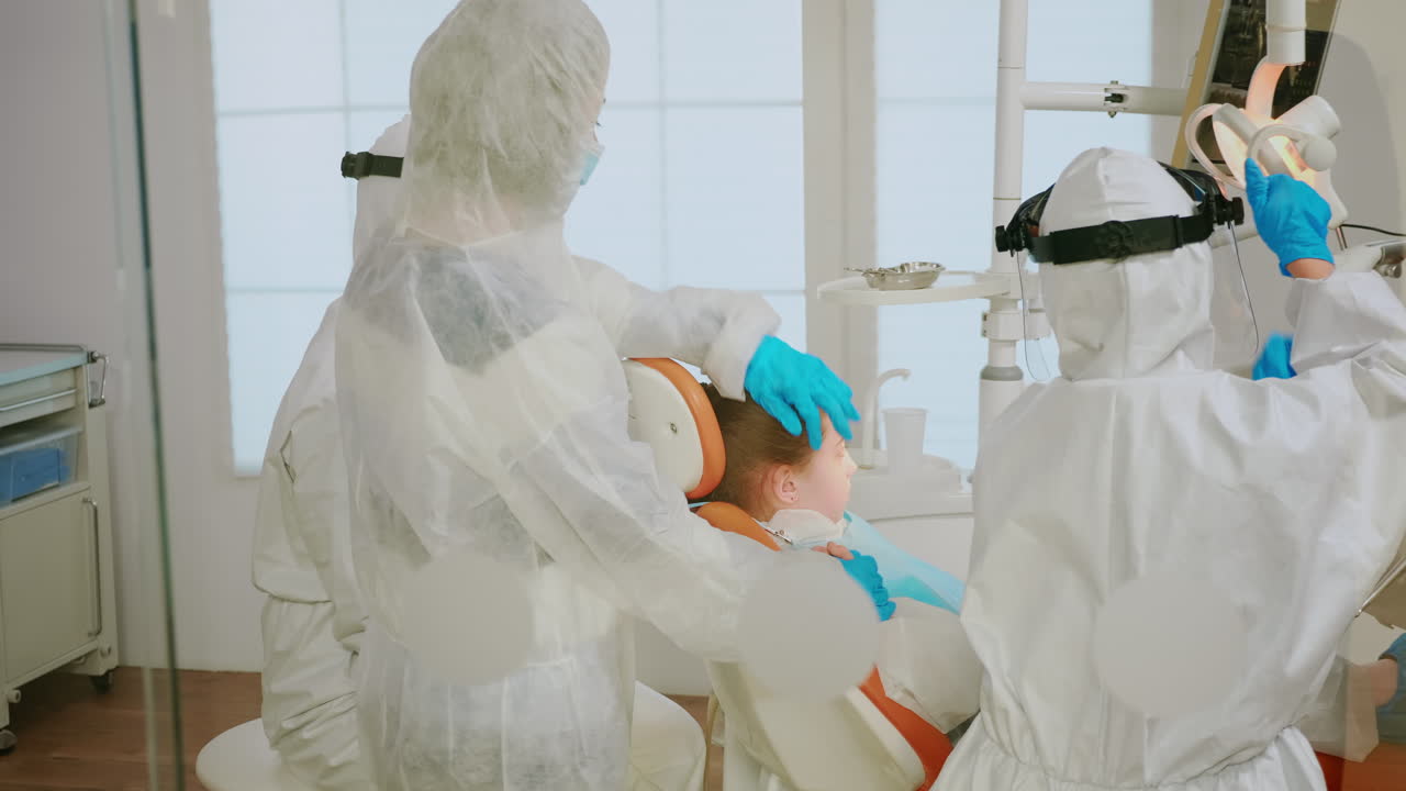 아이 의 치아 를 치료 하는 옷 을 입은 치과 의사 팀 의 뒷면