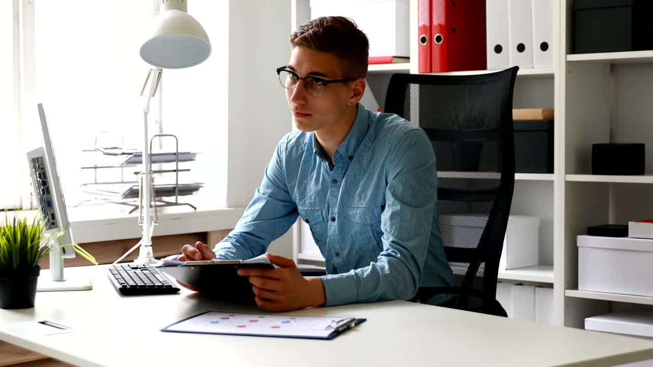 hombre de negocios con gafas, sentado en la mesa y mirando a la cámara