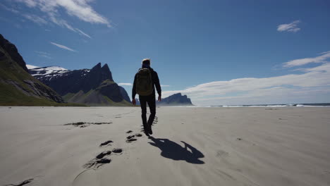 a person walks along a vast sandy beach towards majestic mountains under a blue sky