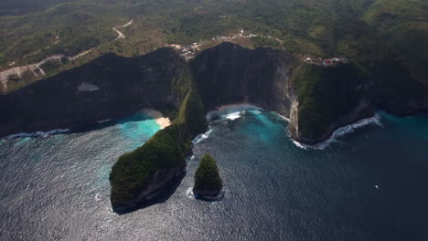 drone flying forward above kelingking beach on nusa penida island over the seashore green peninsula yellow sand