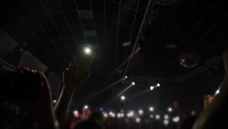 crowd at concert with raised hands holding smartphones capturing vibrant stage lights