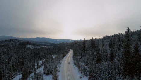 Snowy-Mountain-Road:-A-Following-Shot-of-a-Car-Driving-Along-Little-Fort-Highway-24-Surrounded-by-Wooded-Areas-and-Peaks-in-Sunset-Light
