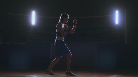 A-beautiful-woman-boxer-trains-in-a-dark-gym-and-works-out-punches-in-slow-motion.-side-view.-Steadicam-shot