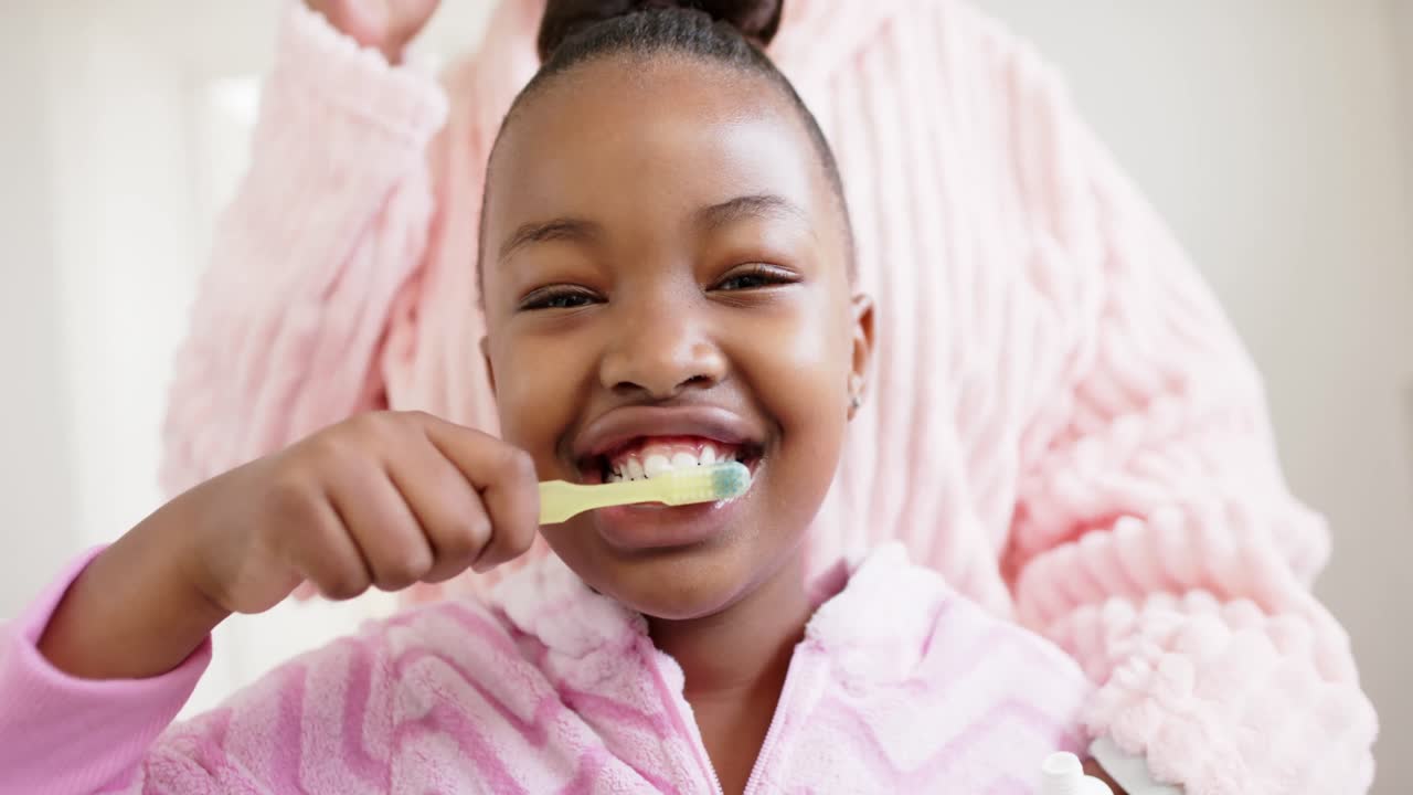 Madre e figlia afroamericane felici si lavano i denti in bagno, al rallentatore