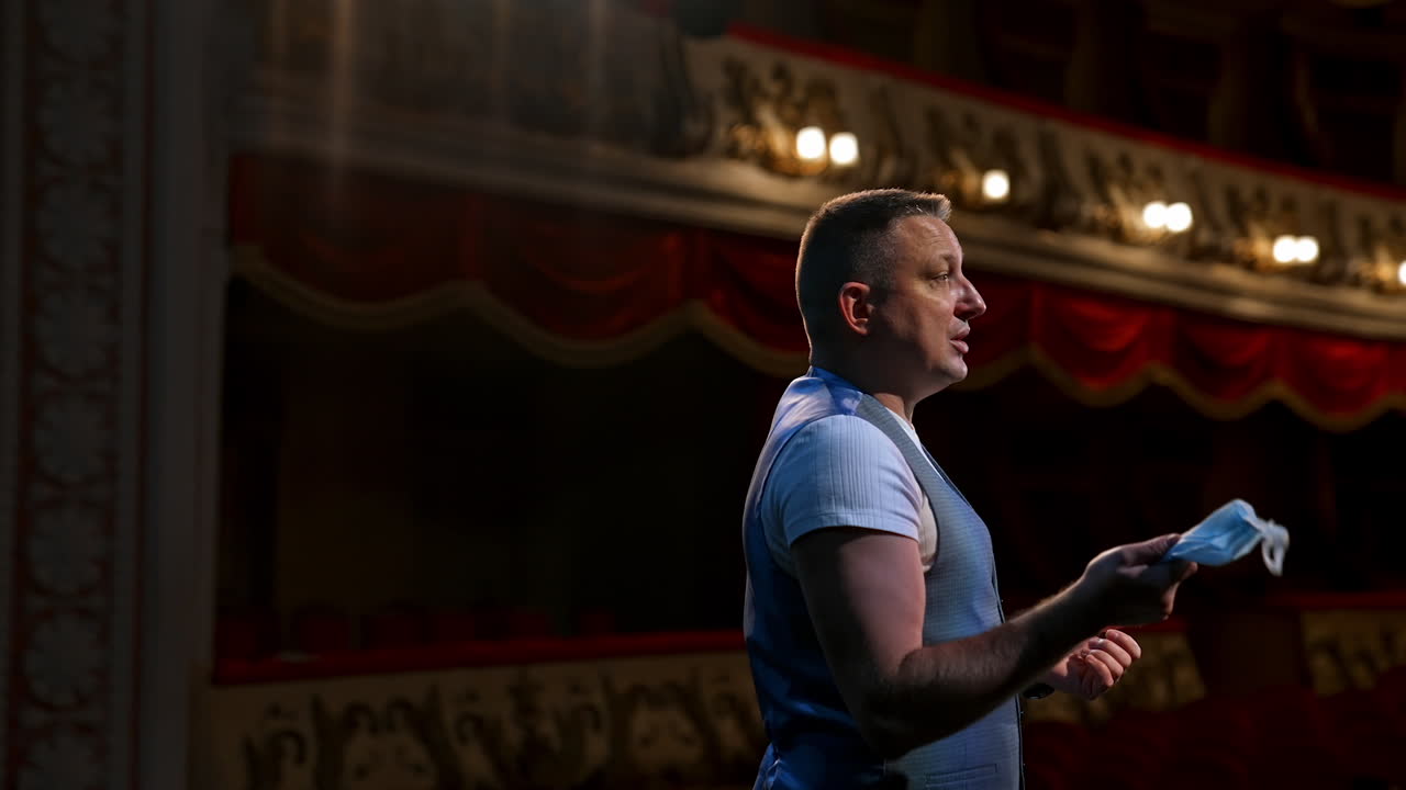 Man with medical mask in hands standing on stage and speaks seriously. Rehearsal during covid-19.