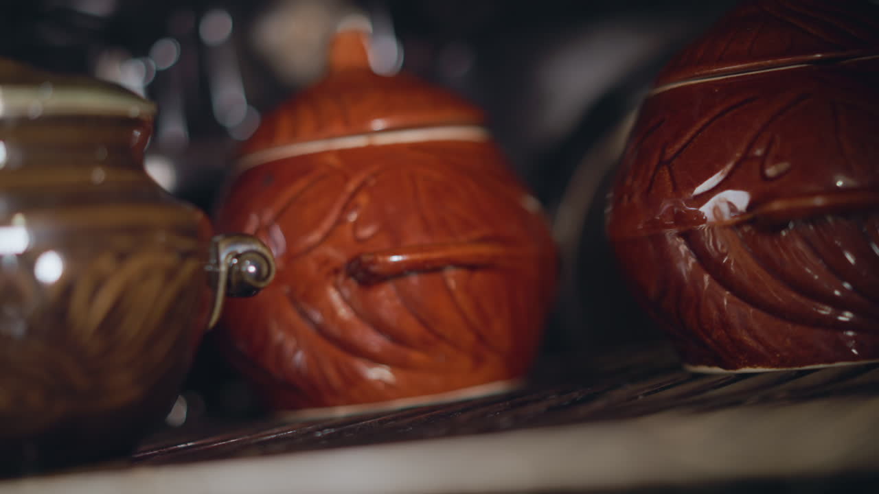 Glazed pots on oven rack, closeup texture. Detailed macro of ceramic surfaces, glossy leaf pattern, shallow depth of field, handcrafted pottery, artisan cooking vibe, intimate food preparation scene