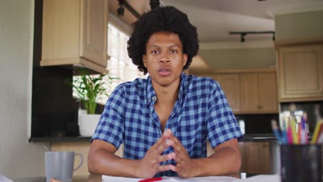 hombre afroamericano serio gesticulando en una videollamada en la cocina