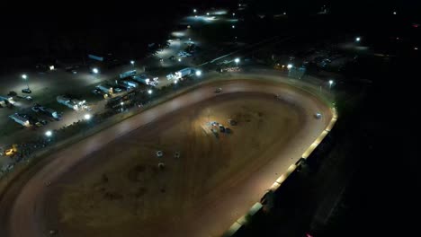 aerial orbit of race car racing on oval dirt track at night