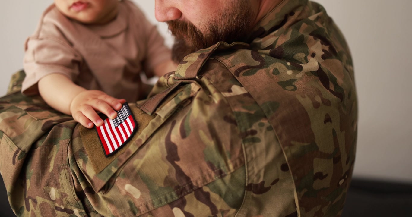 Mano de bebé toca parche de bandera estadounidense en uniforme de soldado