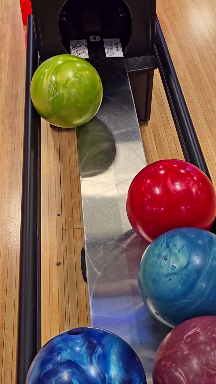 Fixed vertical shot of bowling balls rolling back on the automatic return ramp at a bowling alley