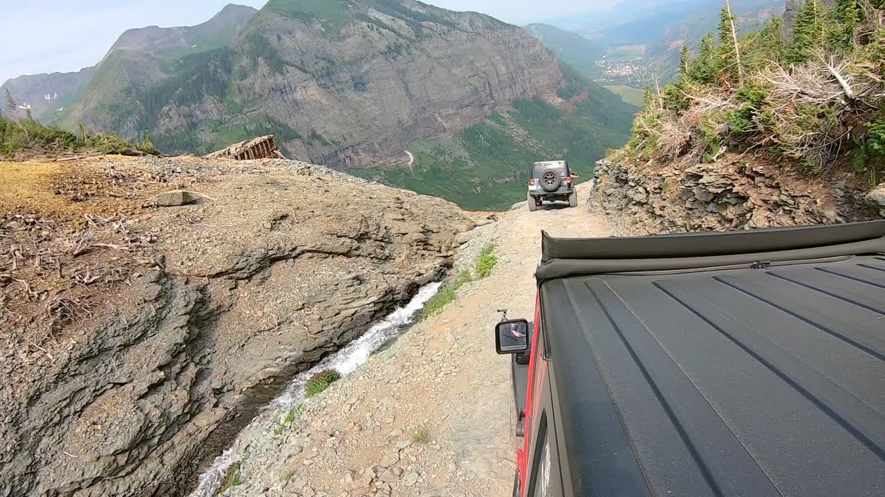 punto de vista desde la azotea de un vehículo 4wd siguiendo a otro en el camino del paso del oso negro a lo largo de ingram creek y pase el edificio de la mina abandonada cerca de telluride colorado