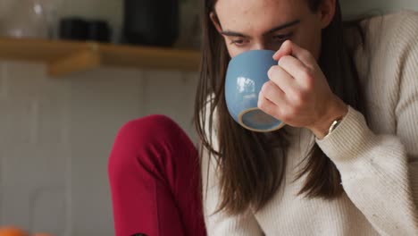 mujer transgénero caucásica no binaria bebiendo café y usando un teléfono inteligente