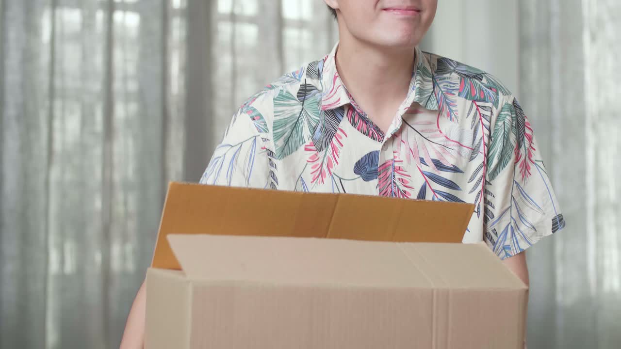un hombre asiático feliz bailando y celebrando termina de llevar una caja de cartón con cosas a una nueva casa. él celebra el día de la mudanza