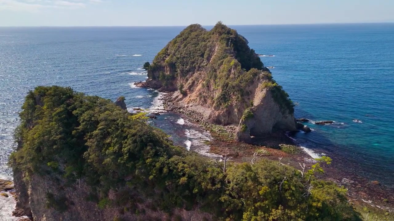 Drone voando de perto sobre os picos arborizados e falésias acidentadas das Ilhas Sanshiro, cercadas pelo límpido Oceano Pacífico azul.