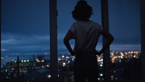 Mujer-Joven-Mirando-Por-La-Ventana-Disfrutando-De-La-Vista-De-La-Ciudad-Por-La-Noche-Contemplando-Un-Estilo-De-Vida-Exitoso-Planificando-Con-Anticipación-En-Una-Tranquila-Tarde-Urbana