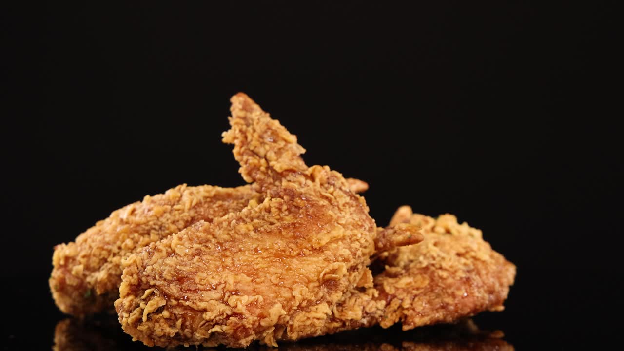 Golden-brown fried chicken wings rotate smoothly on a glossy black surface, illuminated by soft studio lighting for appetizing texture and detail