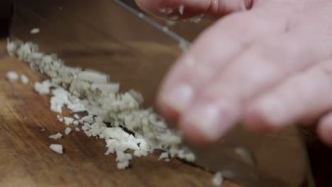 Man-finely-cuts-garlic-with-a-knife-on-a-wooden-board