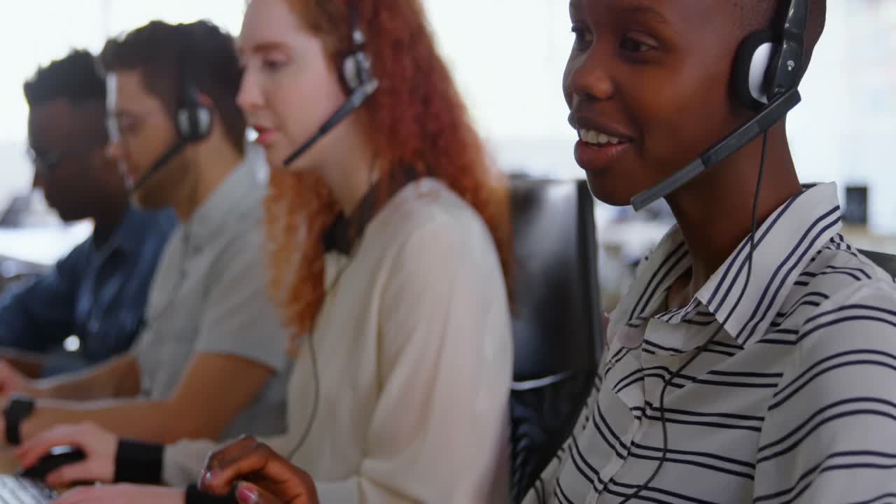 Side view of young cool mixed-race call center team calling and sitting at desk of modern office 4k