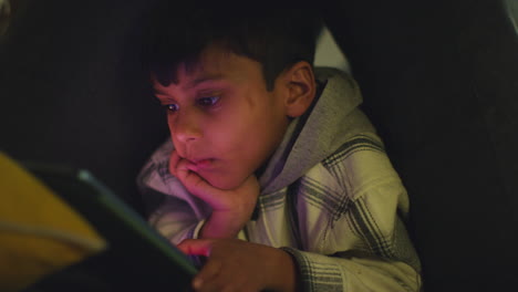 Close-Up-Of-Young-Boy-In-Home-Made-Camp-Made-From-Cushions-Playing-With-Digital-Tablet-At-Night-3