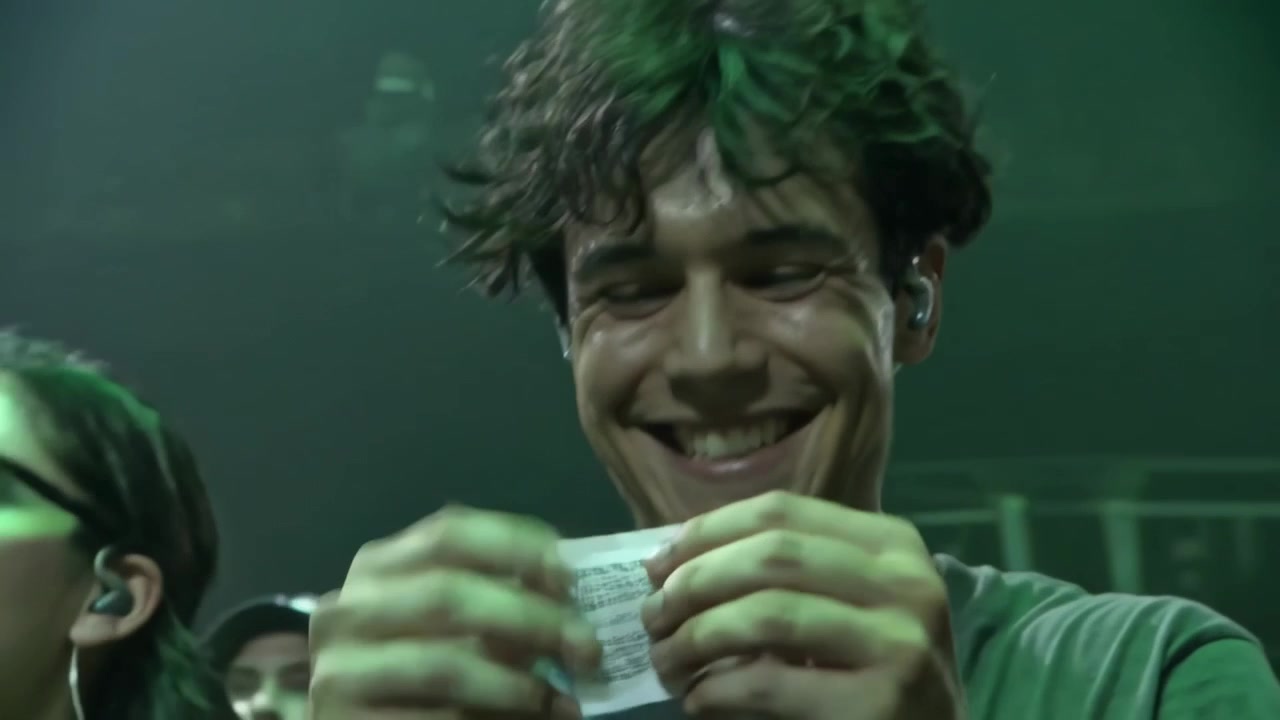 Smiling adult male wearing green tee examining printed paper, tearing and crumpling it near stage