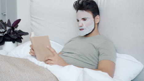 man reading a book in bed with a face mask