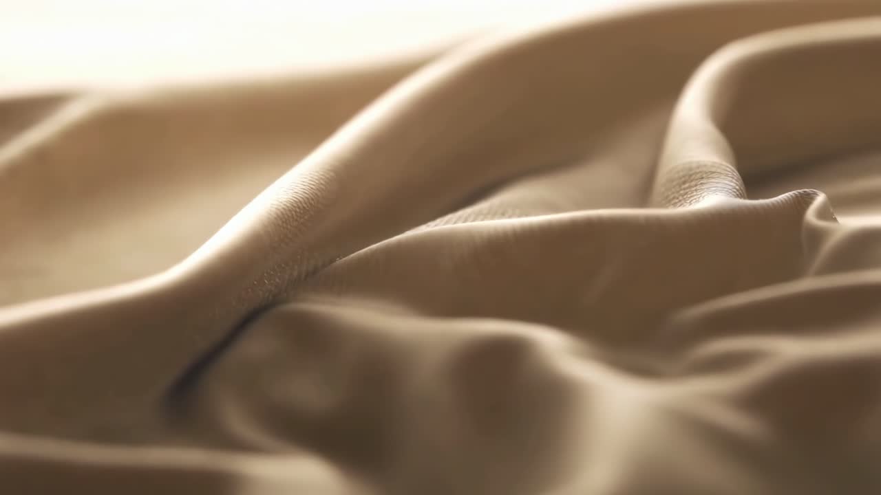 Close-up video of smooth, flowing beige fabric, captured from a low angle for texture