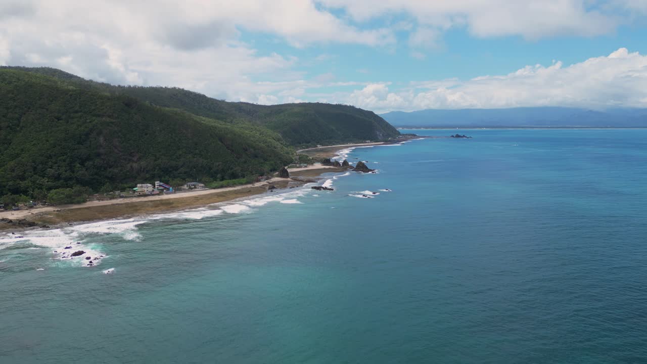 A stunning shot showcases lush green landscapes meeting the tranquil shoreline, with the vast ocean stretching beneath a clear blue sky.