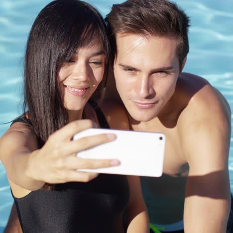 una pareja guapa toma una foto mientras está de pie en la piscina