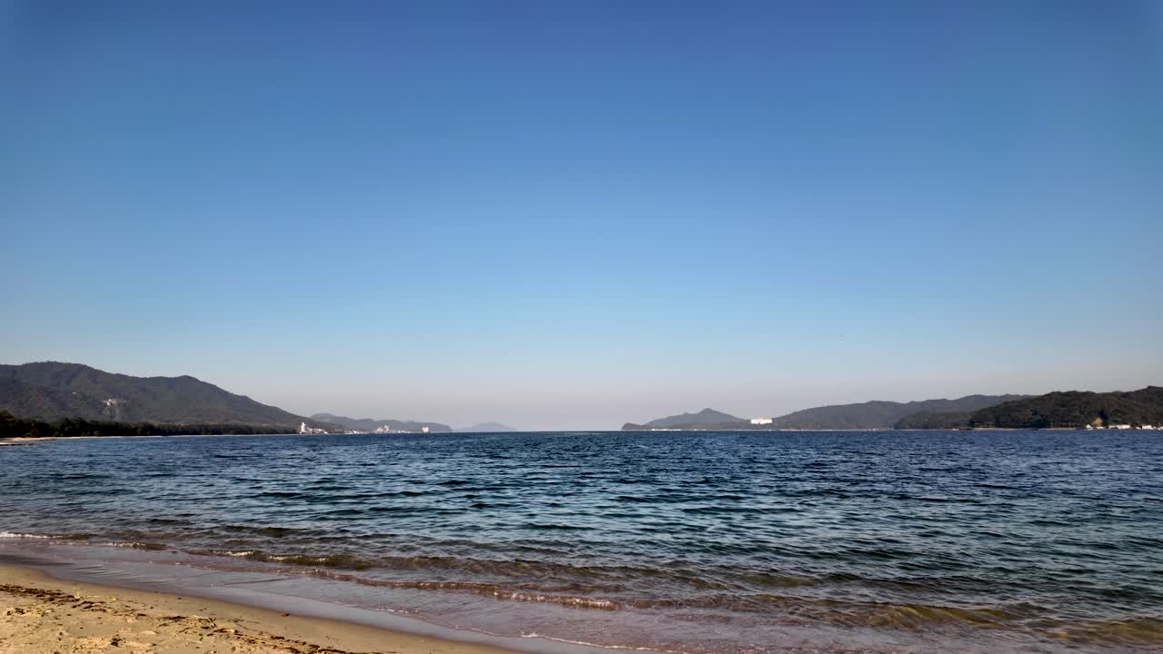 Calm sea waves gently lapping the sandy shore of Amanohashidate beach on a clear sunny day in Miyazu Bay, Japan. Pan right shot