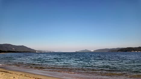 calm sea waves gently lapping the sandy shore of amanohashidate beach on a clear sunny day in miyazu bay, japan. pan right shot