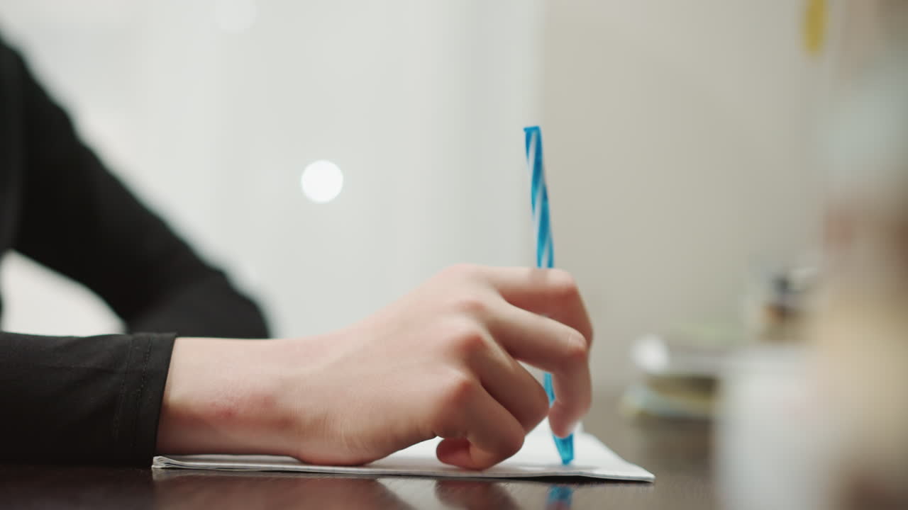 Closeup of hand with writing instrument. Person contemplating with pen and journal in soft warm setting. Artist thoughtfully scribbling ideas in journal during peaceful moment of reflection