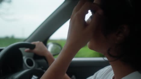 a young asian woman driving her car along a countryside road, talking and gently removing hair from her face