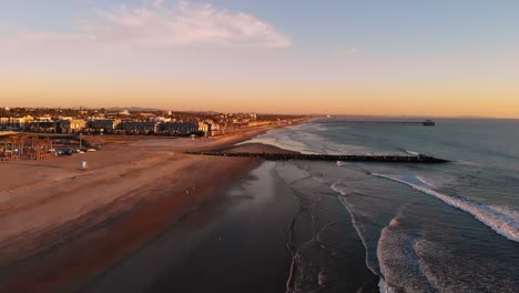 Drohnenaufnahme-Des-Strandes-Und-Krachende-Wellen-Während-Eines-Glühenden-Sonnenuntergangs,-Während-Die-Drohne-über-Das-Wasser-Gleitet