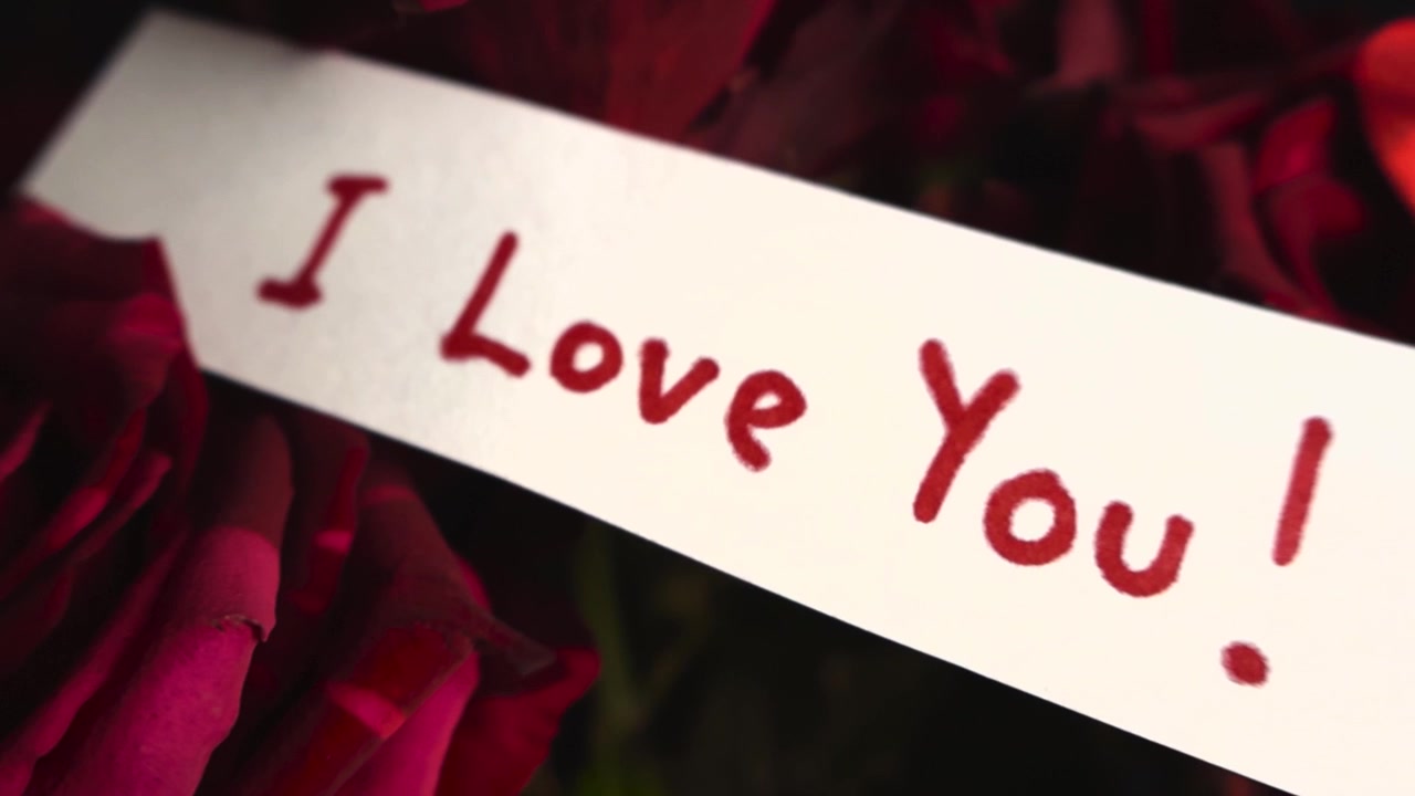 Close-up pesan "I Love You" tulisan tangan pada catatan putih yang diletakkan di atas buket mawar merah yang indah. Konsep hadiah yang sempurna untuk Hari Valentine, ulang tahun, atau lamaran.