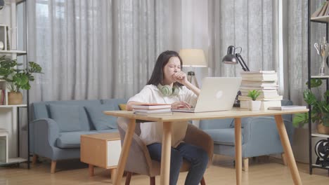 teenage girl yawning while studying on laptop at home