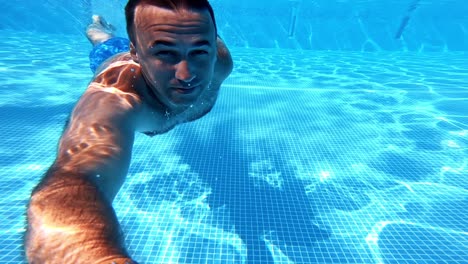 man underwater in the pool. healthy man swimming inside the blue clear water of the swimming pool and looking to camera. summer vacation.