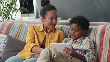 Afroamerikanischer-Junge-Benutzt-Tablet-Und-Chattet-Mit-Mama-Auf-Dem-Sofa-Zu-Hause