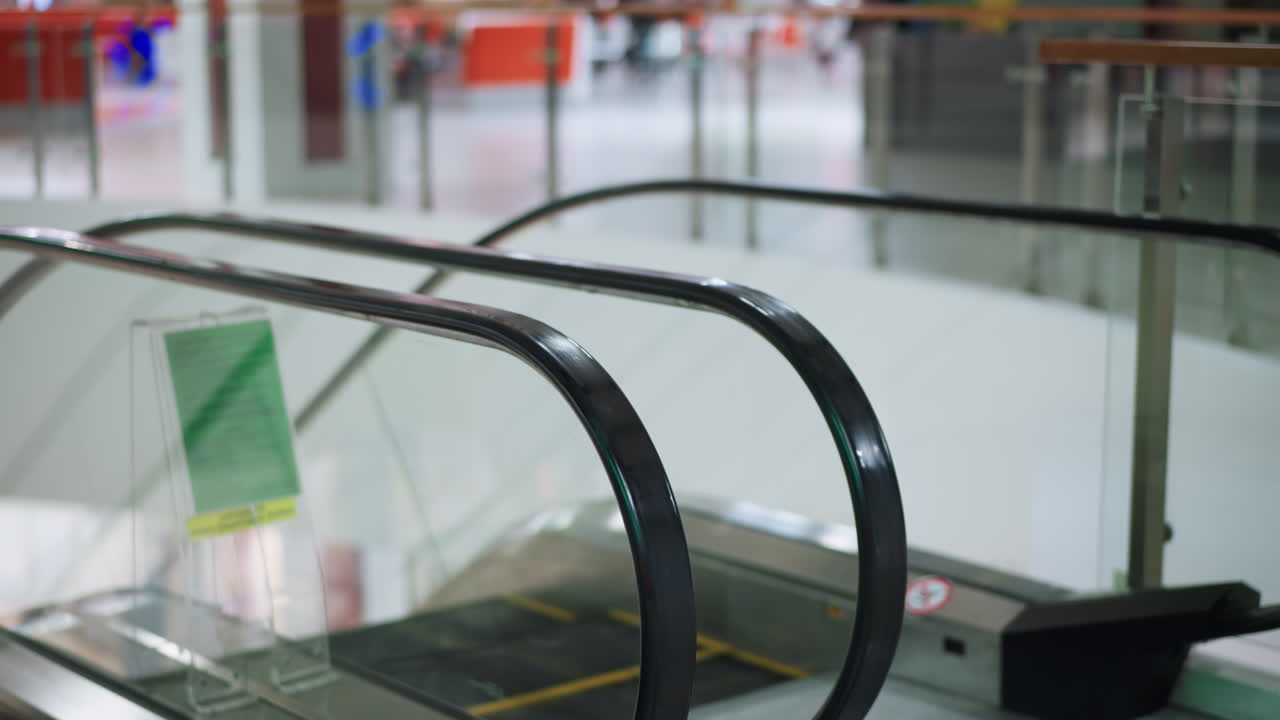 Empty escalator indoors in shopping mall with blurred background, metal rails, glass panels, and modern flooring, showing transport infrastructure, urban lifestyle and architecture