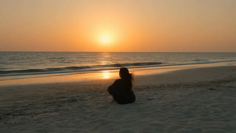 person watches a beautiful sunset over the ocean from a sandy beach