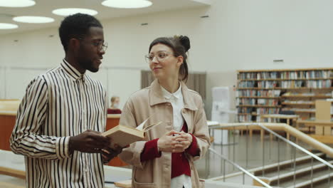 diverse man and woman walking in library and chatting