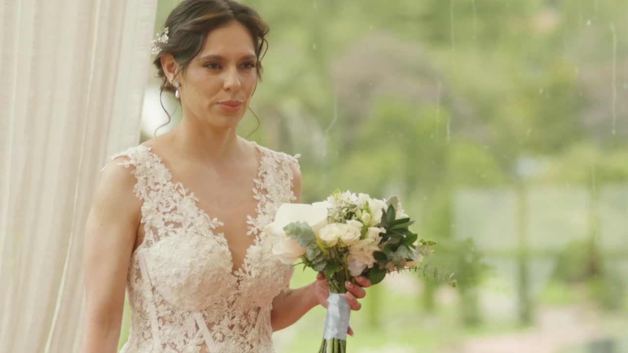 Medium shot of a bride walking with a bouquet of flowers, wearing a lace dress as she heads to the ceremony.