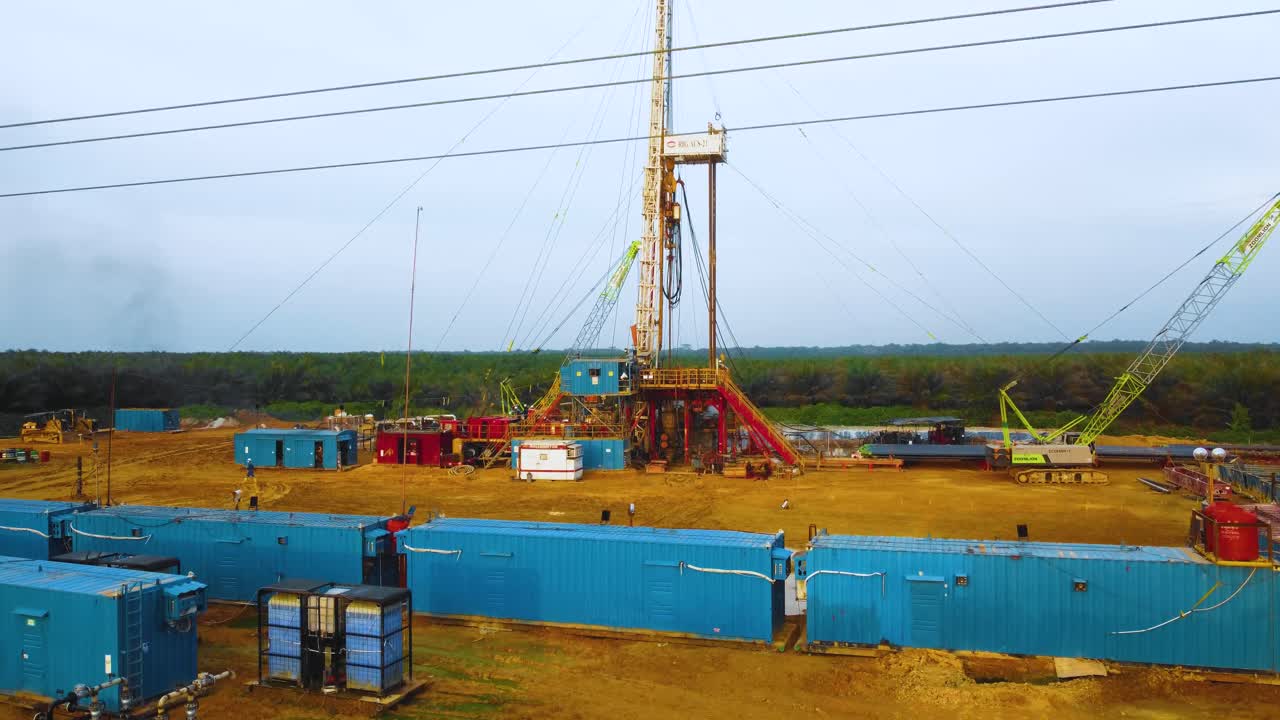 imágenes cinematográficas de drones de la estructura del equipo de la plataforma de perforación en tierra para la exploración y explotación de petróleo en medio de la jungla rodeada de palmeras durante la puesta de sol y el alto precio del petróleo